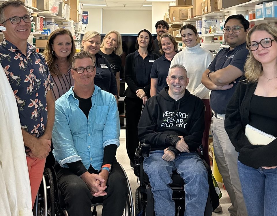 Group of people in a laboratory, two people in the wheelchair surrounded by other supporters.