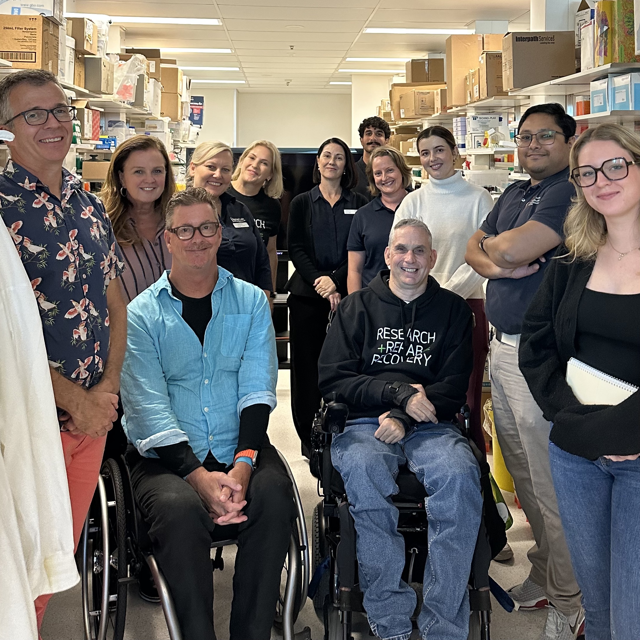Group of people in a laboratory, two people in the wheelchair surrounded by other supporters.