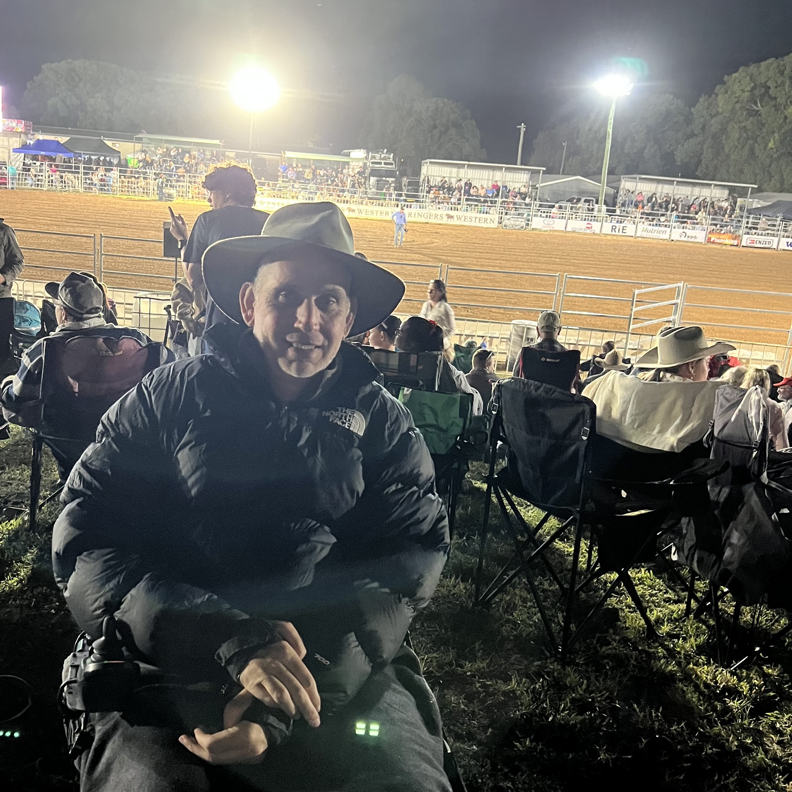 A person with a black jacket, a cowboy hat in the wheelchair, background of a rodeo.